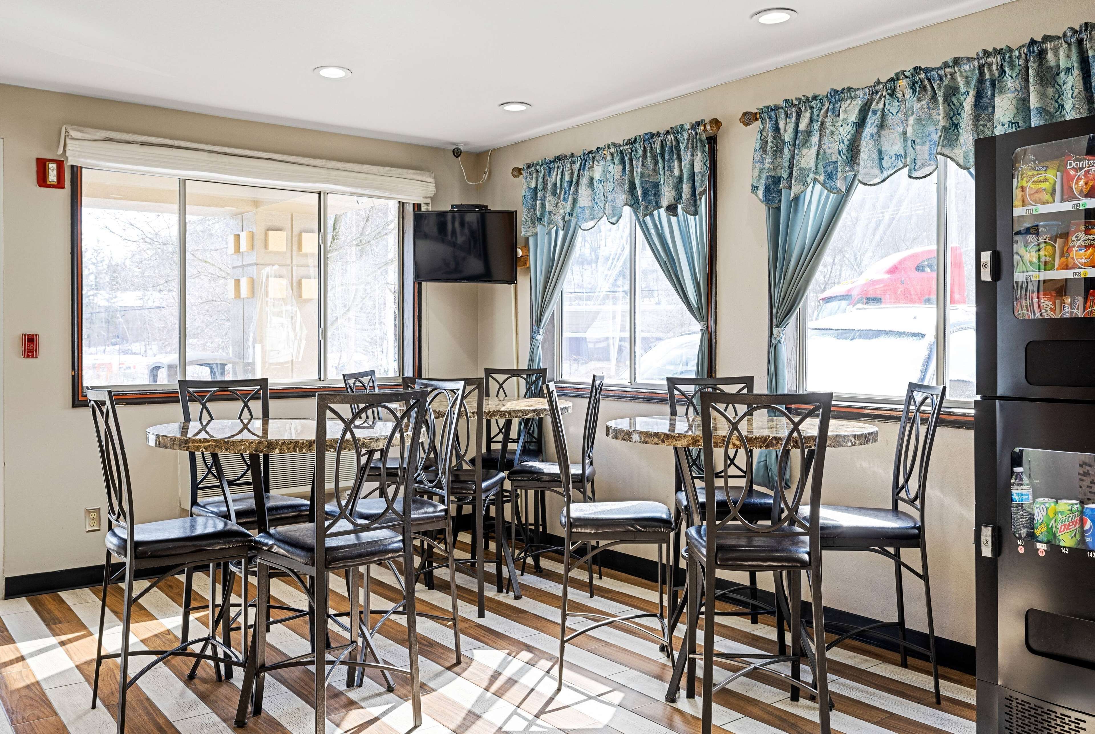 Un comedor con varias mesas y sillas, ventanas amplias con cortinas y una máquina expendedora de aperitivos.