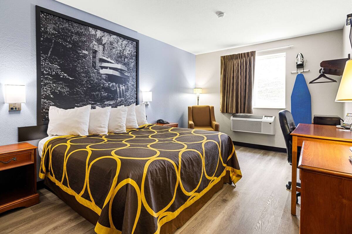A hotel room with a large bed, a desk, a chair, a hanging coat rack, and a window with curtains.