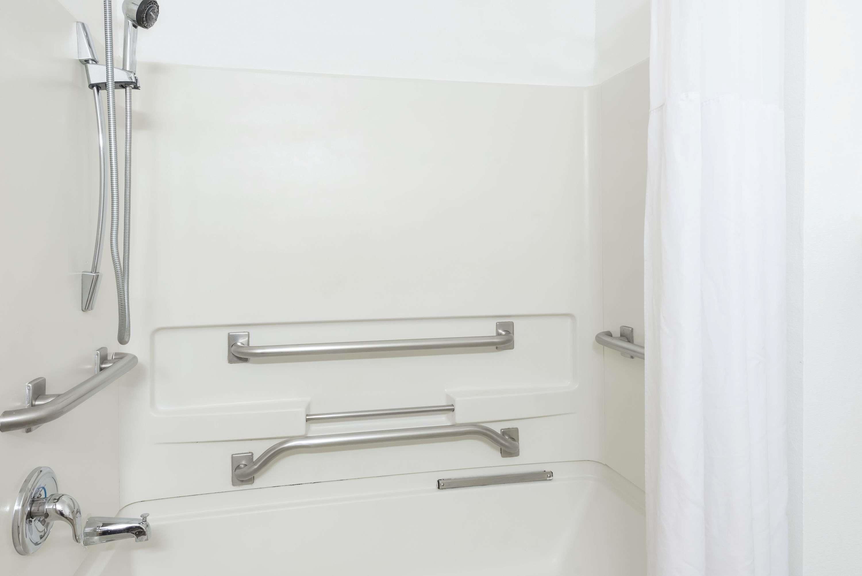 Un baño con ducha a nivel, barras de apoyo y cabezal de ducha manual.