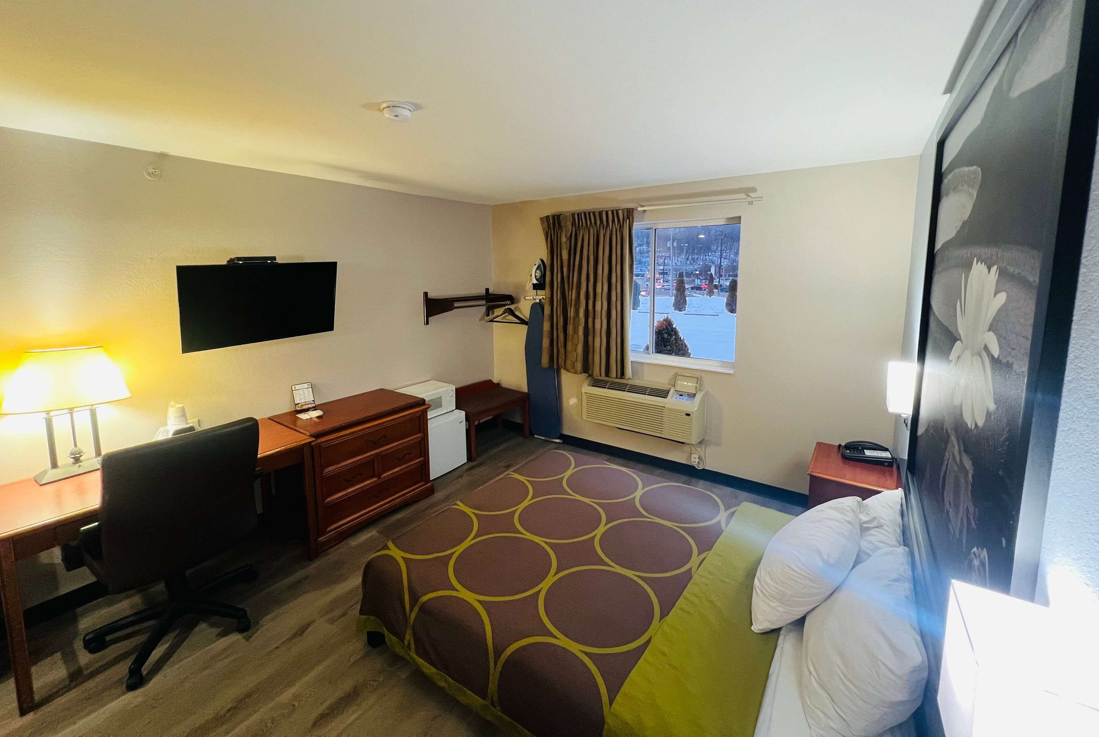 A hotel room with a bed, desk, chair, television, and a window with a view of a snowy landscape.
