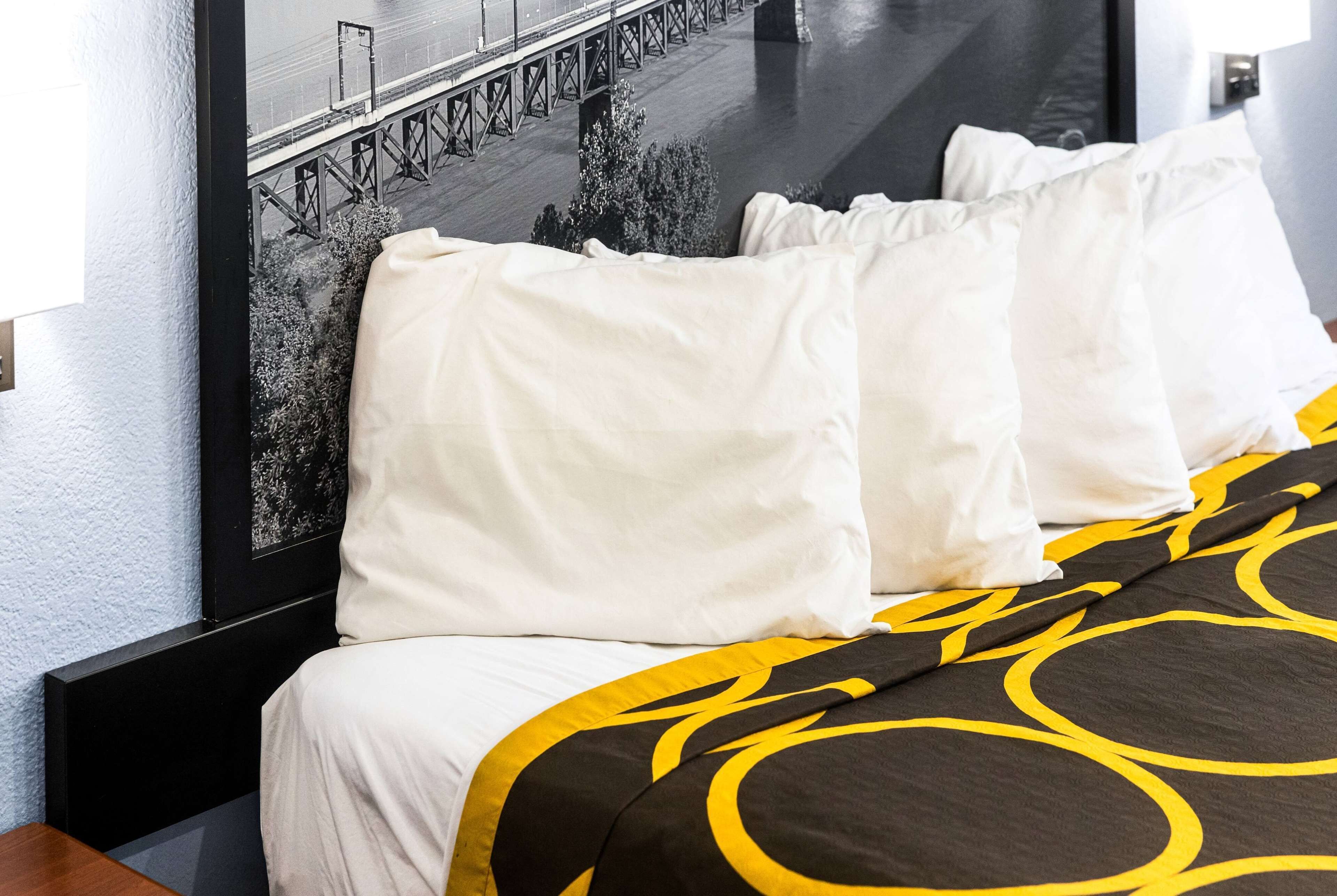 A hotel room with a bed featuring a black and yellow patterned bedspread, white pillows, and a large framed picture of a bridge on the wall.