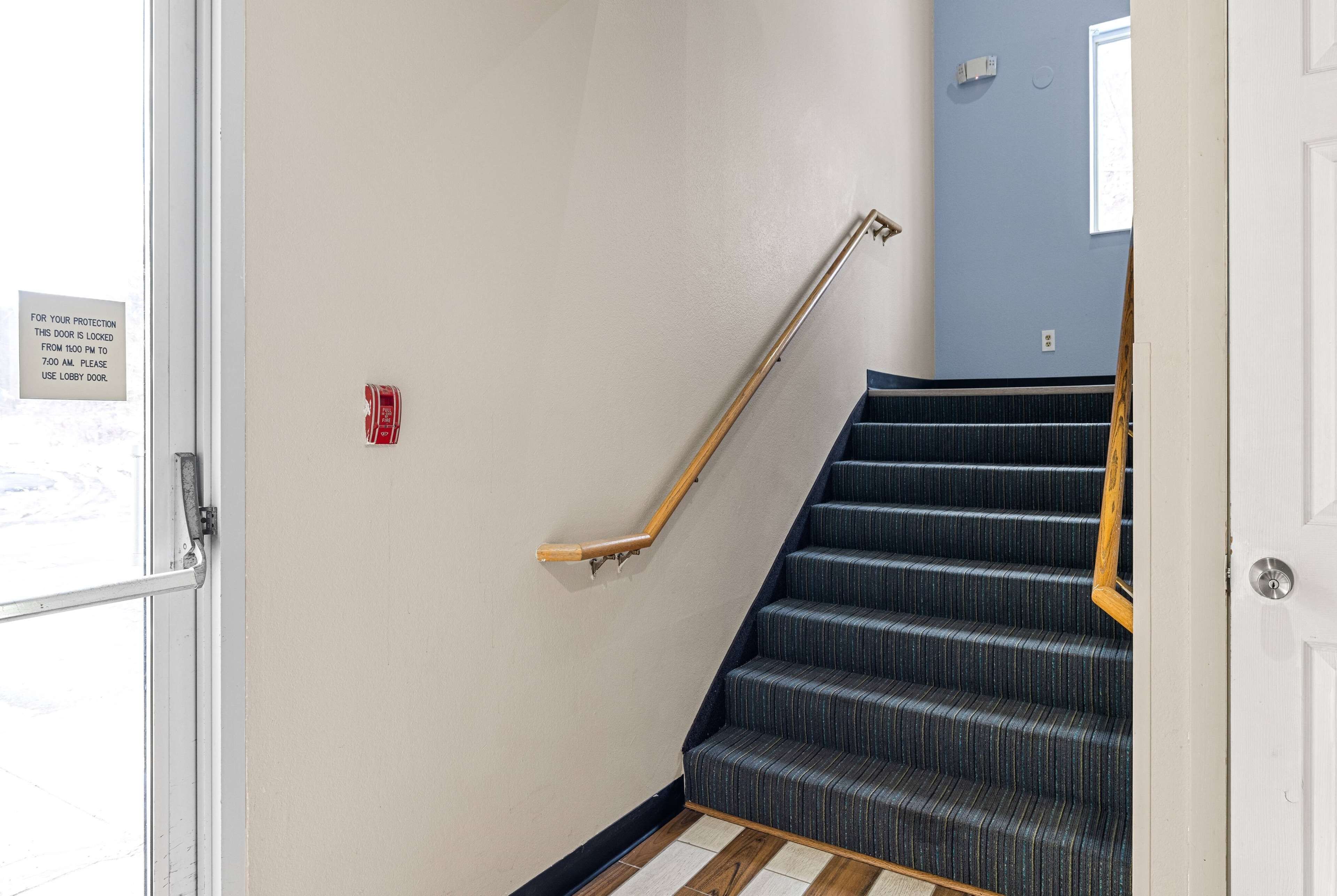 A staircase with a wooden handrail and a fire alarm on the wall.