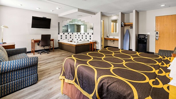 A hotel room with a large bed, a sofa, a desk with a computer, a TV, a bathroom with a mirror, and a microwave. - Super 8 by Wyndham Pittsburgh/Monroeville (Pittsburgh)