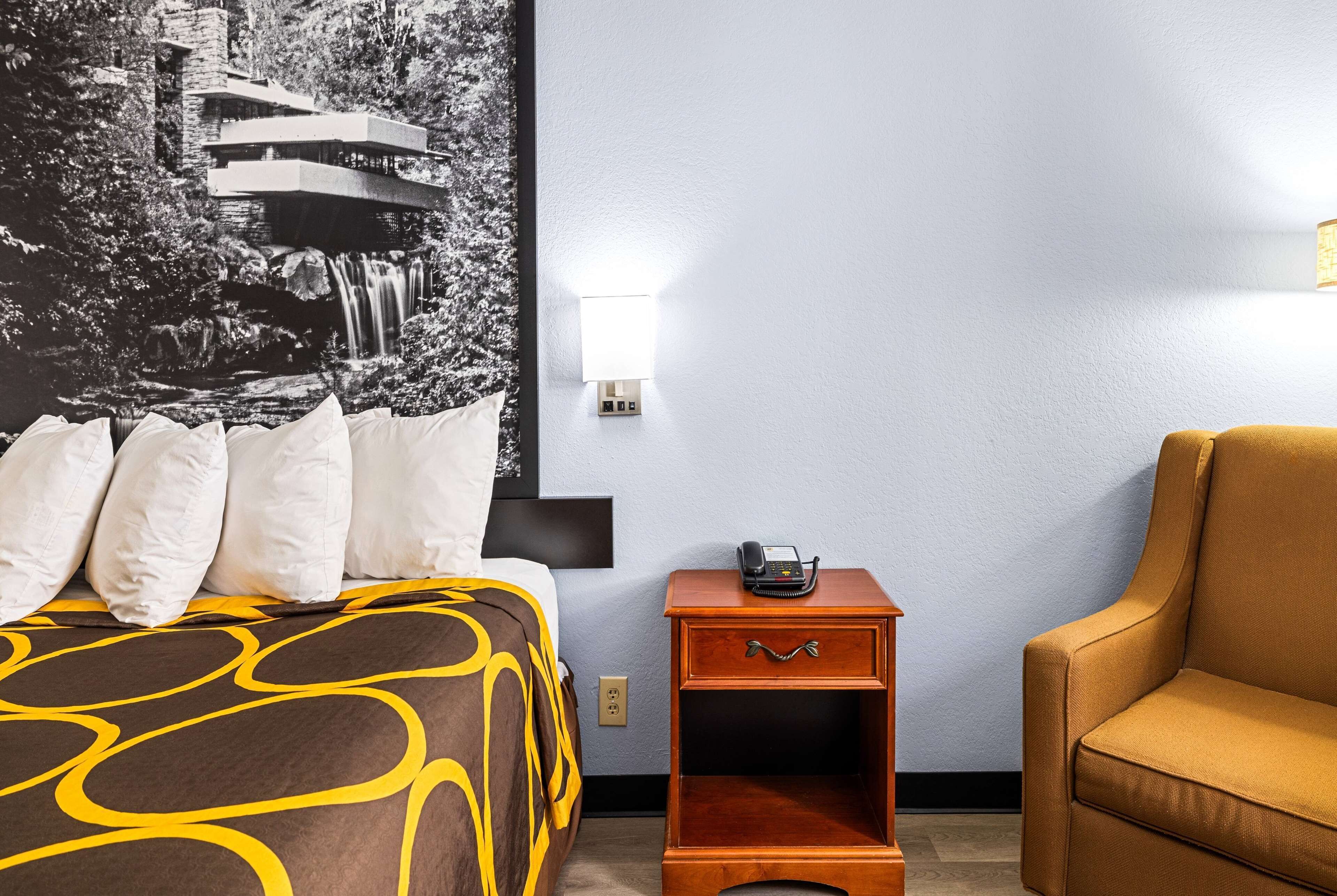 A hotel room with a bed, a nightstand, a lamp, and a chair.