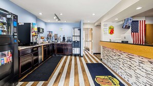 A modern kitchen with stainless steel appliances, a microwave, and a water dispenser. There is a wooden floor with a striped pattern and a blue rug with a logo. - Super 8 by Wyndham Pittsburgh/Monroeville (Pittsburgh)