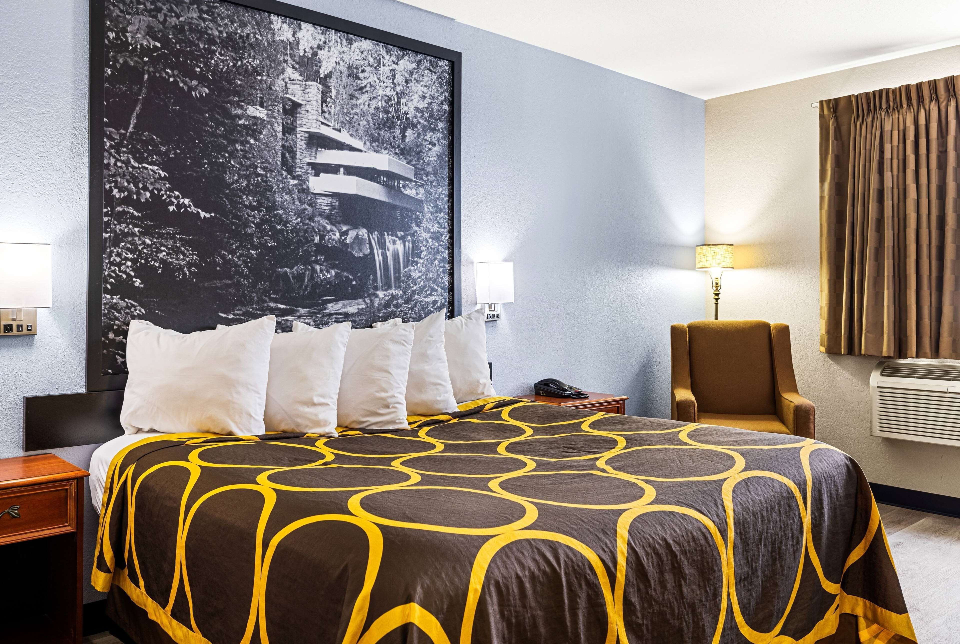 Quarto de hotel com uma cama grande, uma cadeira, uma escrivaninha e ar condicionado fixado na parede.