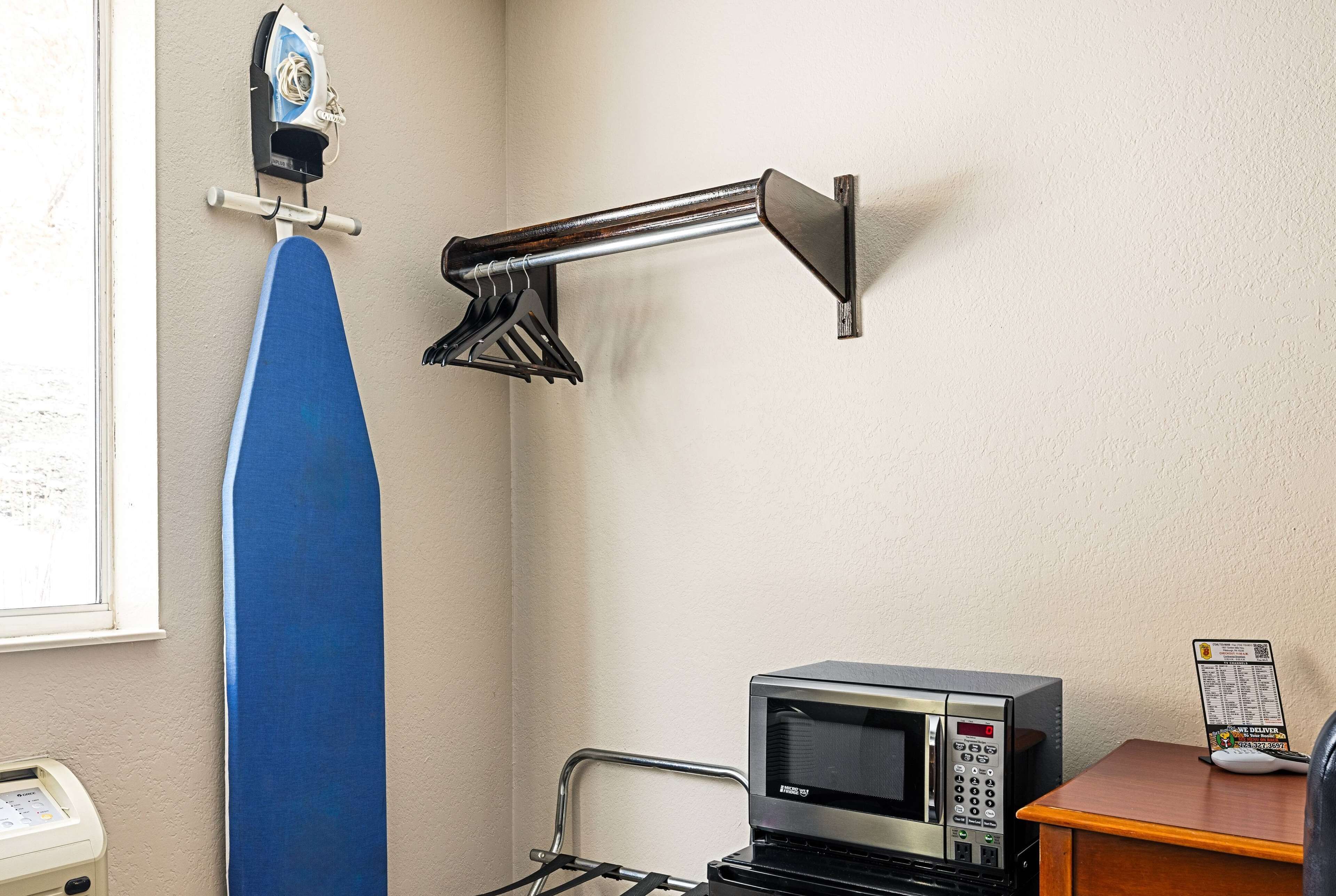 A room with a blue ironing board, a microwave, and a small table with a menu.