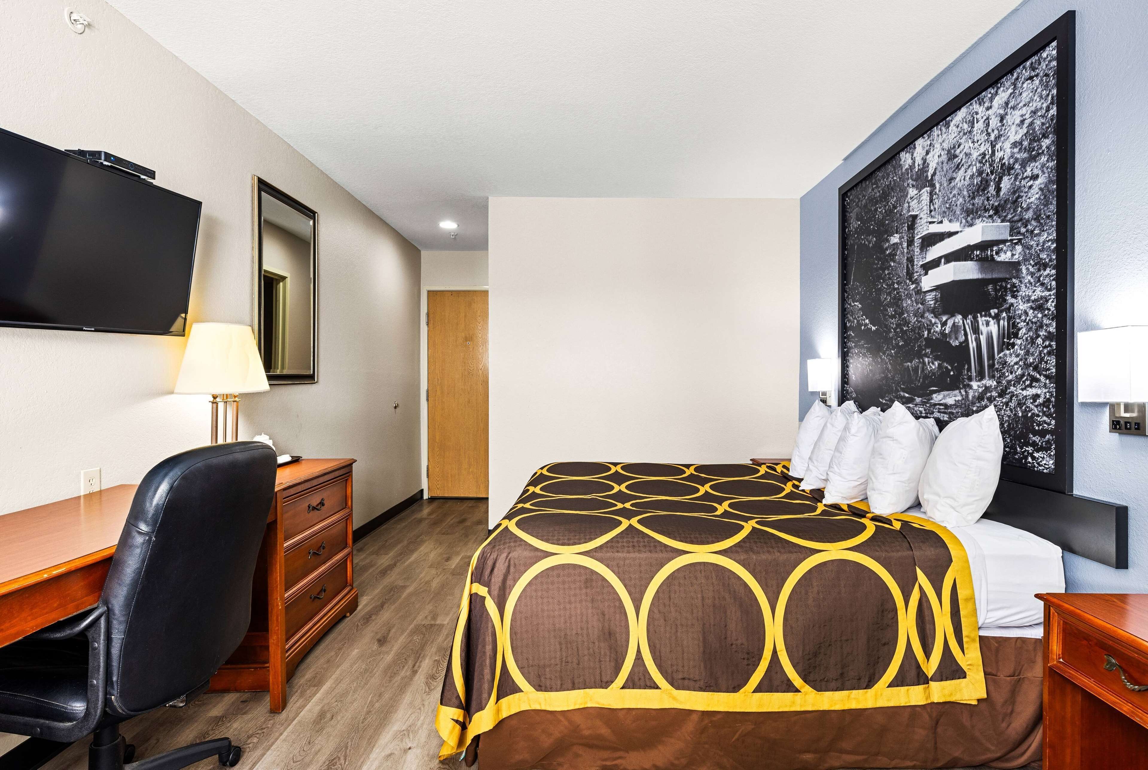 A hotel room with a bed, a desk, a chair, a TV, and a large painting on the wall.