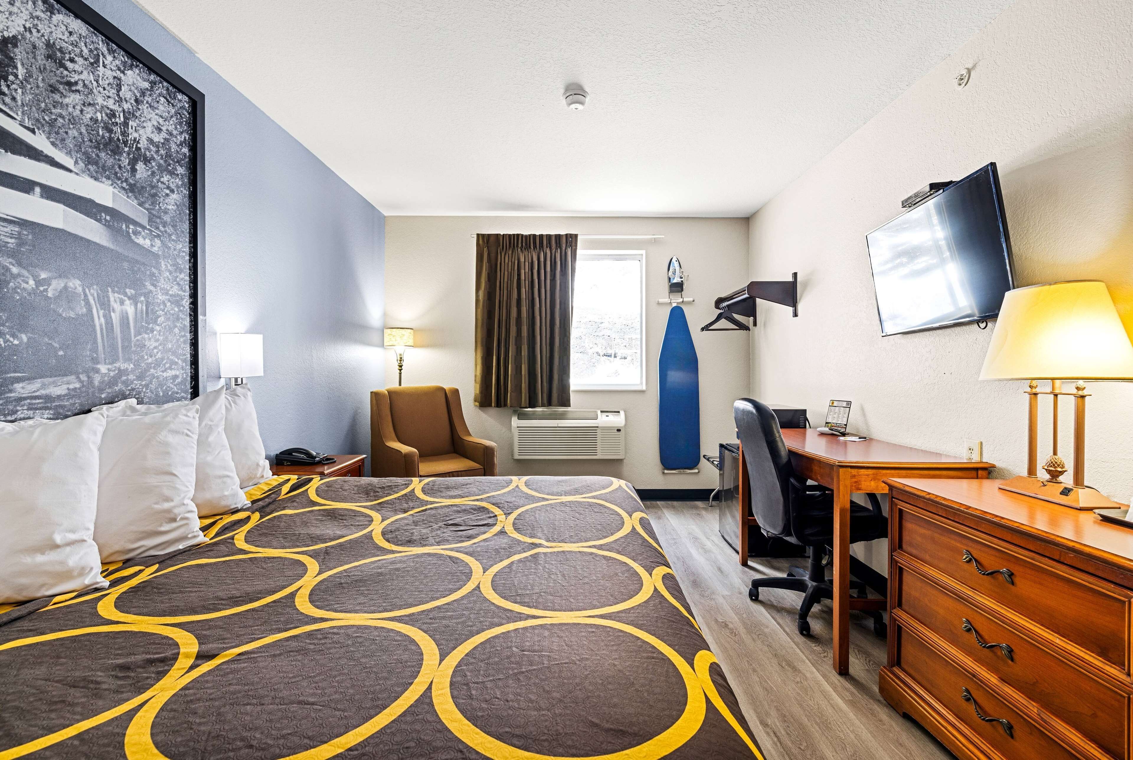 A hotel room with a large bed, a desk, a chair, a TV, and a window with curtains.