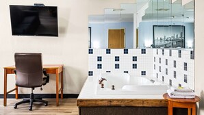 A hotel room with a wooden desk, a brown office chair, a large flat-screen TV, a white bathtub, and a tiled wall with a cityscape mirror. - Super 8 by Wyndham Pittsburgh/Monroeville (Pittsburgh)