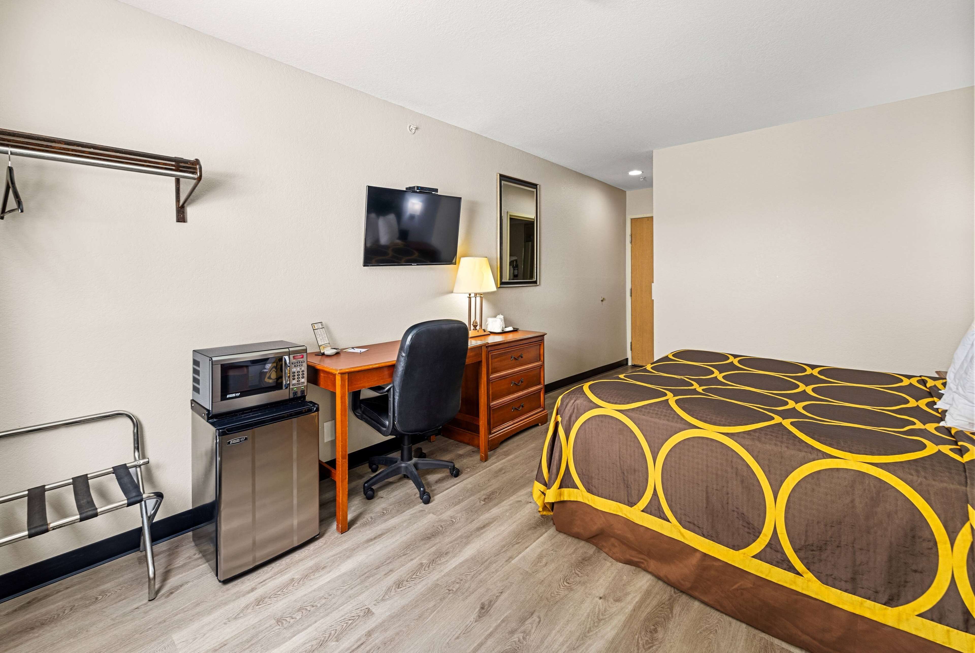 Ein Hotelzimmer mit einem Bett, einem Schreibtisch mit Computer, einer Mikrowelle, einem Stuhl, einem kleinen Kühlschrank, einem Fernseher und einem Spiegel.