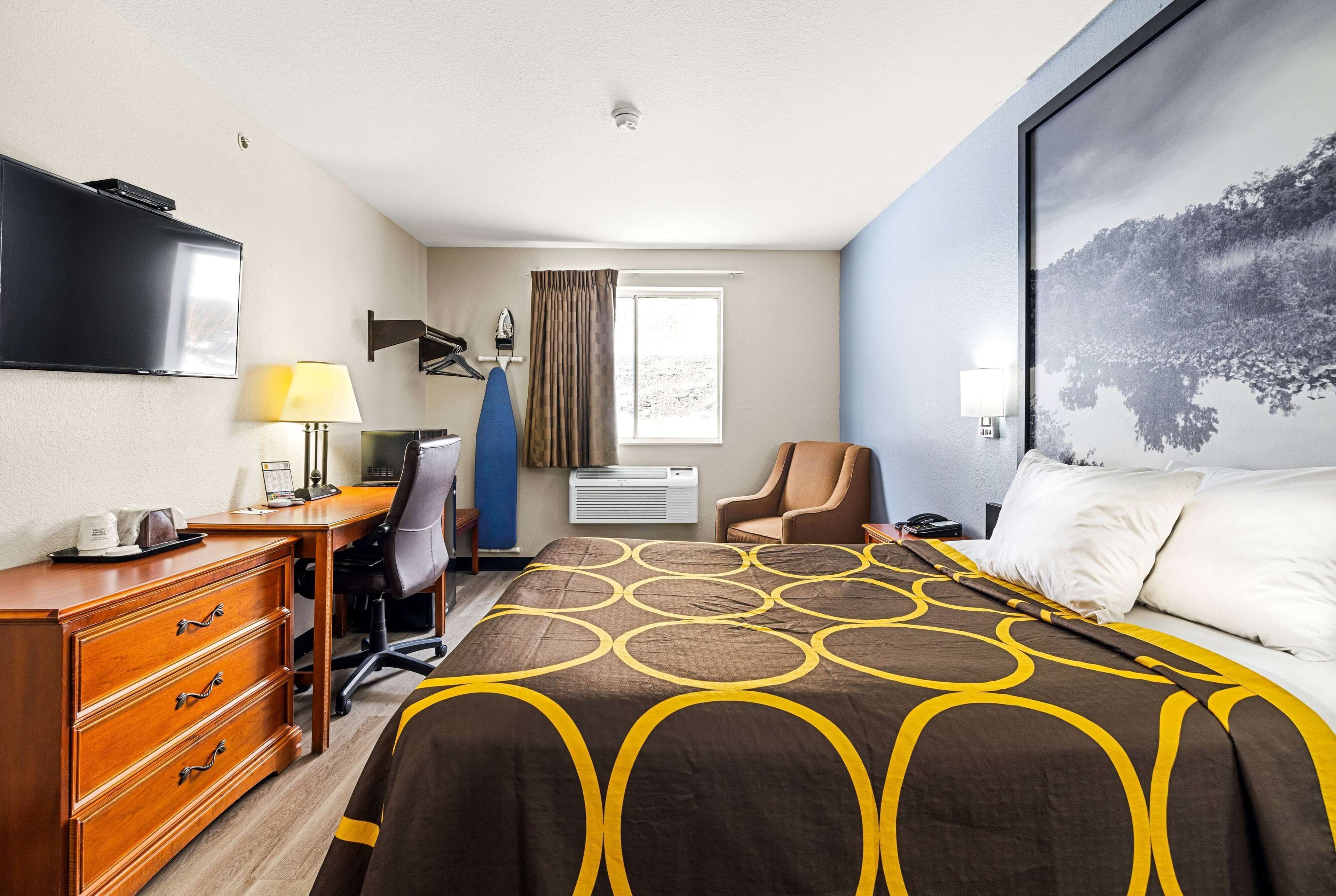 Quarto de hotel com cama, escrivaninha, cadeira, televisão e janela com cortinas.
