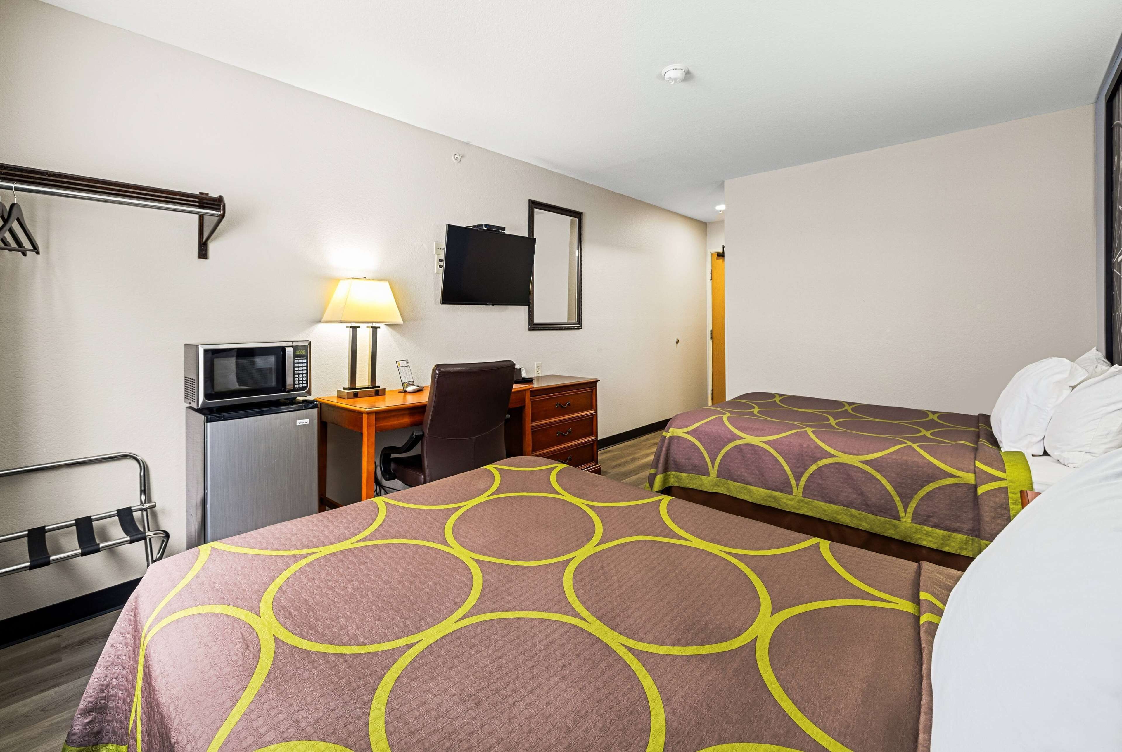 Quarto de hotel com duas camas, uma escrivaninha com computador, televisão e luminária.