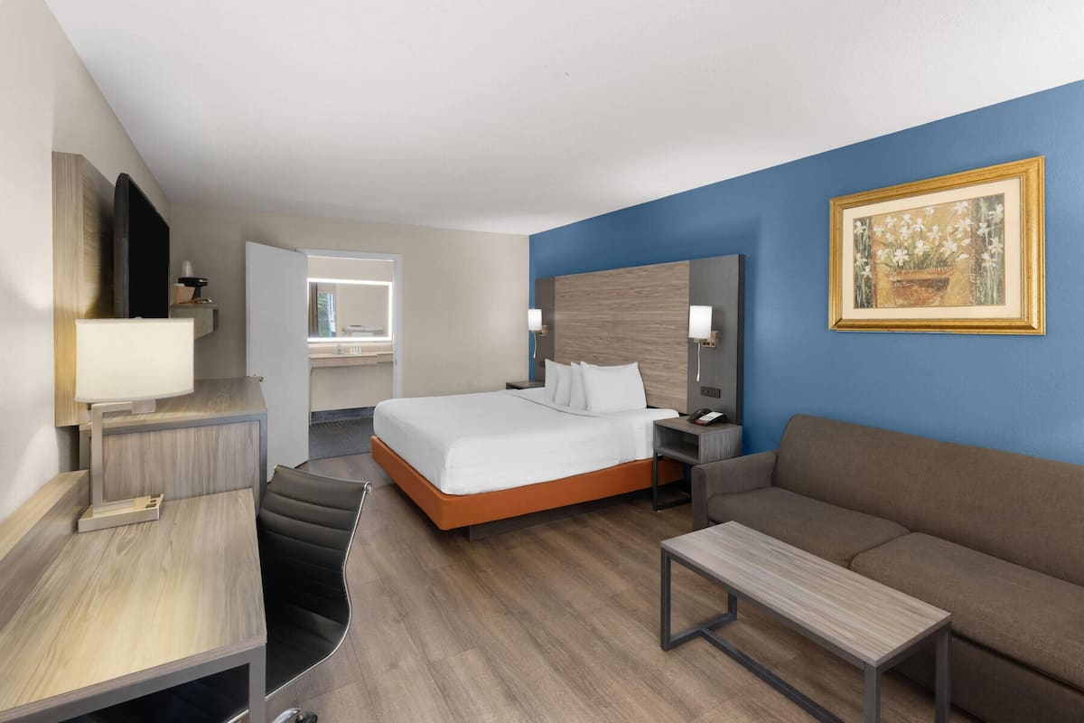 A modern hotel room with a bed, a desk, a sofa, and a TV.