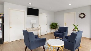 Una habitación con dos sillones azules, una mesa redonda, un televisor de pantalla plana en la pared y una planta en maceta.