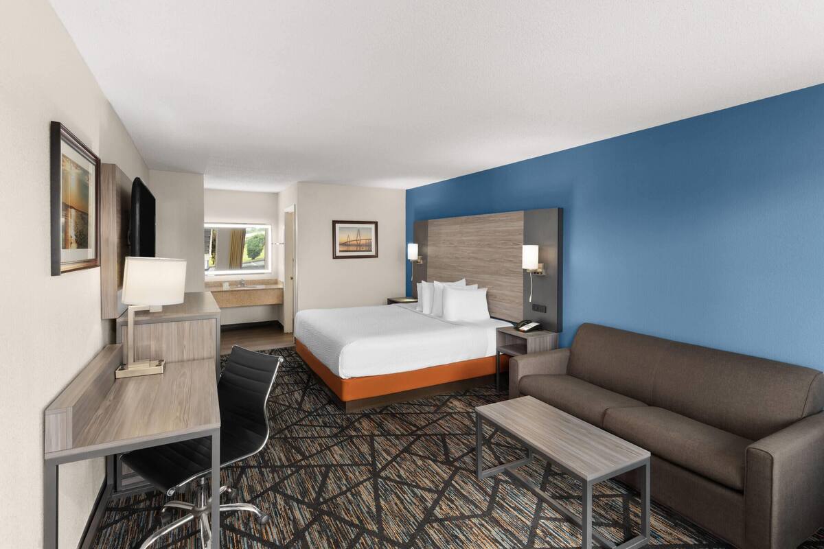 A hotel room with a bed, a desk with a chair, a sofa, and a small table.