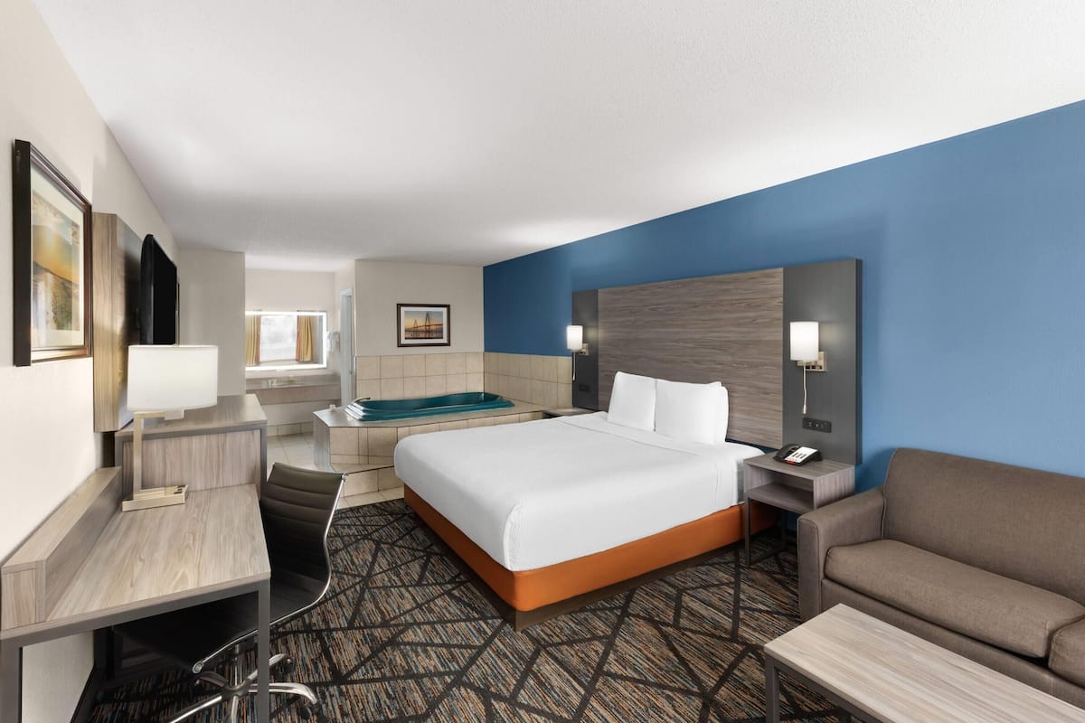 A hotel room with a bed, a desk, a chair, a sofa, a desk lamp, a nightstand, a telephone, and a window with curtains.