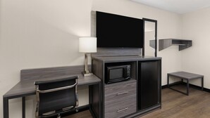 Una habitación de hotel compacta con kitchenette, televisor de pantalla plana, escritorio con silla y una mesita pequeña.