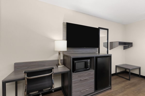 A compact hotel room with a kitchenette, a flat-screen TV, a desk with a chair, and a small table.