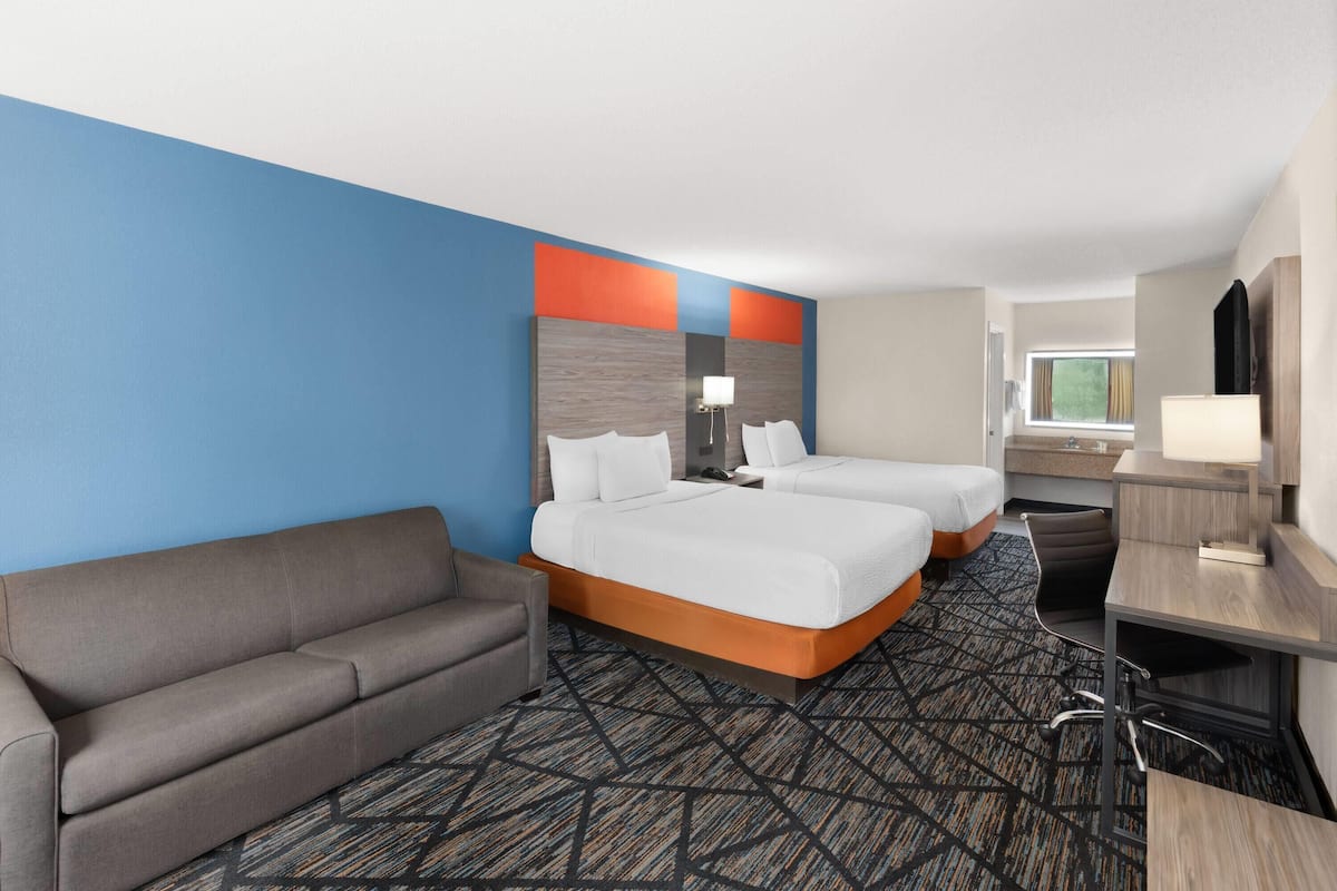 A hotel room with two beds, a sofa, a desk, and a bathroom.