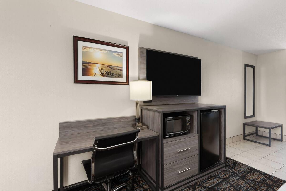 A hotel room with a desk, chair, flat-screen TV, microwave, and a small table.