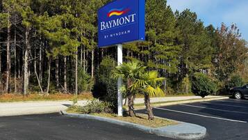 Señal de un hotel llamado 'Baymont by Wyndham', con un estacionamiento y árboles al fondo.