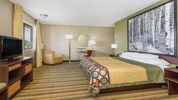 A hotel room with a bed, a TV, a desk, a chair, a lamp, and a large forest-themed painting on the wall.