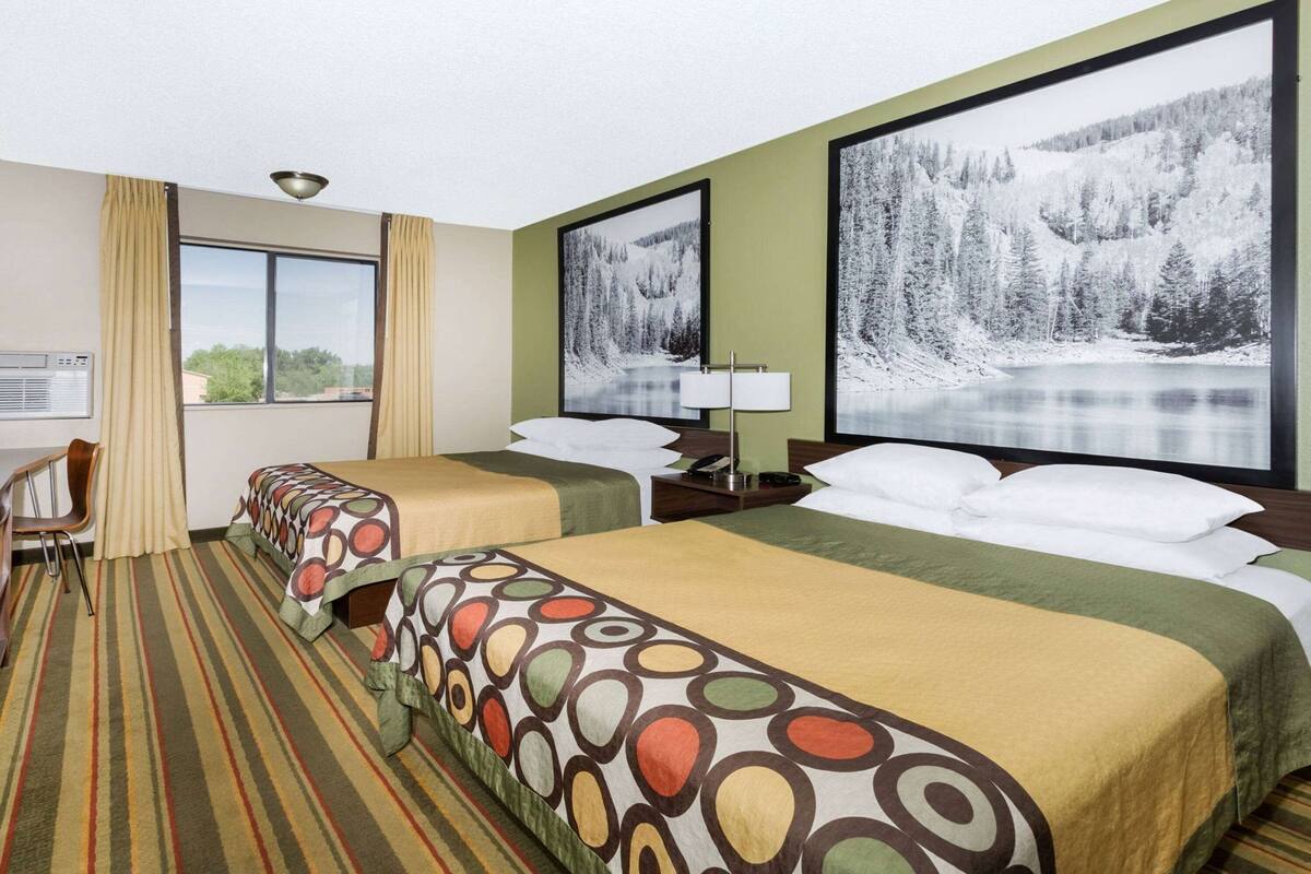 Ein Hotelzimmer mit zwei Betten, einem Schreibtisch, einem Sessel und großen Fenstern mit Blick auf eine verschneite Landschaft.