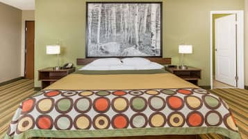 A hotel room with a large bed, two bedside tables with lamps, a framed forest photograph on the wall, and a green carpet.