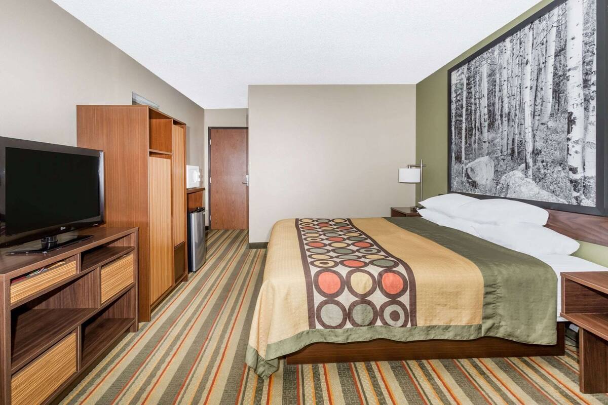 Ein Hotelzimmer mit Bett, Fernseher, Schreibtisch und Kleiderschrank.