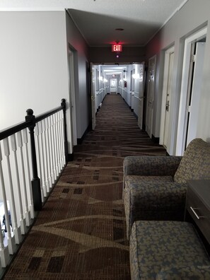 A hotel hallway with carpeted flooring, a staircase with white balusters, and a row of doors on one side. - Adams Inn (Adams)