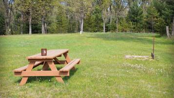 Et picnicbord i en græsmark med træer i baggrunden.
