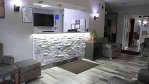 A reception area with a stone wall, a flat-screen TV, and a reception desk. There are two patterned armchairs and a small table with a plant. - Adams Inn (Adams)