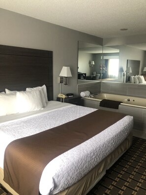 A hotel room with a large bed, a bathroom with a bathtub, a mirror, and a nightstand with a lamp.