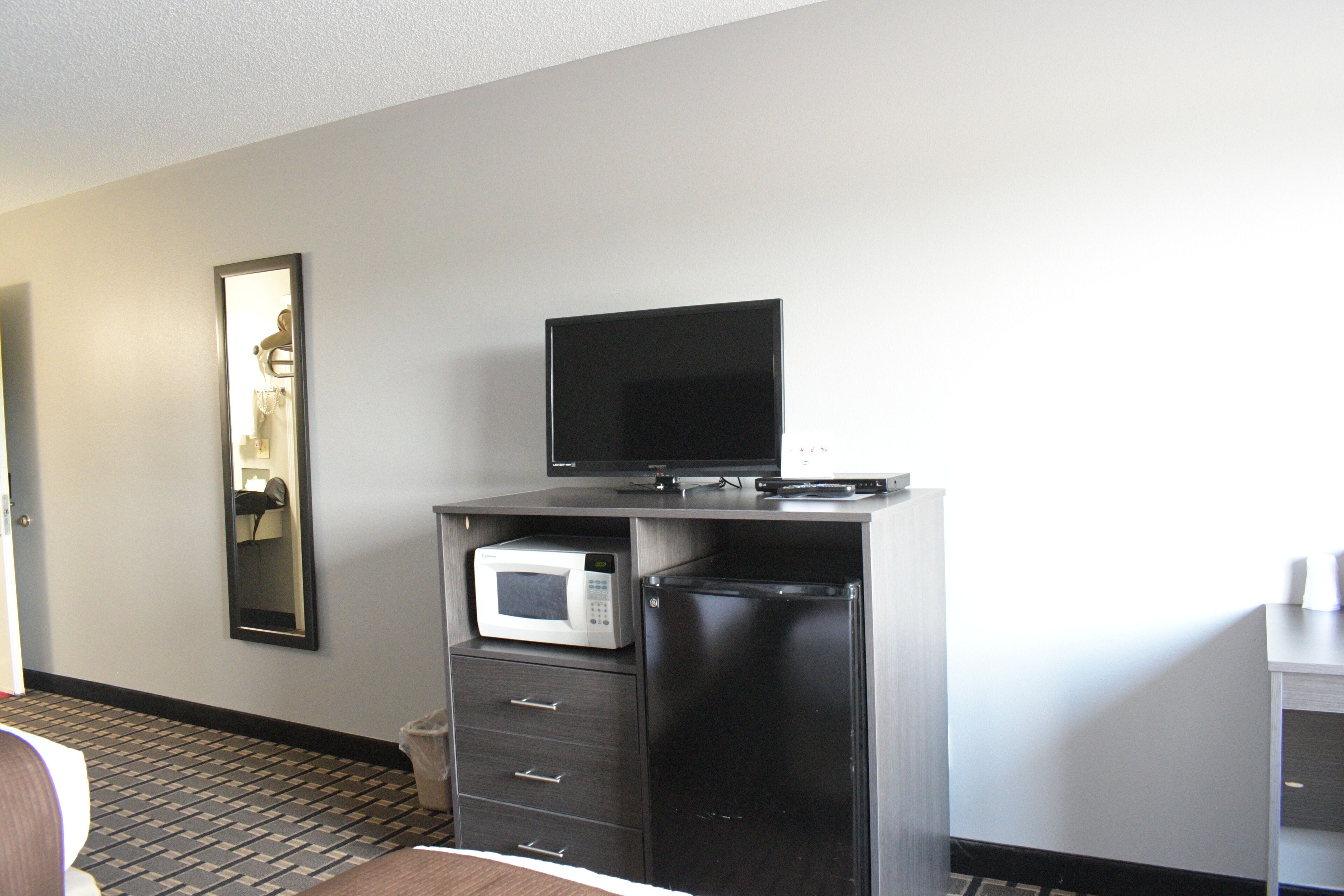 Habitación de hotel con televisor de pantalla plana sobre un mueble, microondas y un cubo de basura.