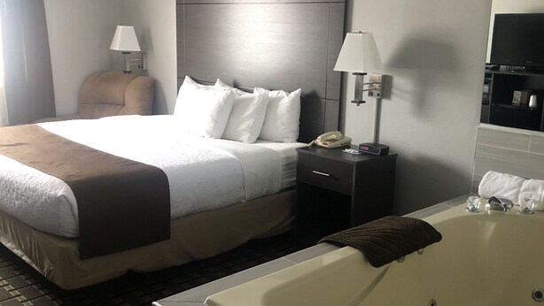 A hotel room with a large bed, a bedside table with a lamp, a telephone, and a bathtub. - Adams Inn (Adams)