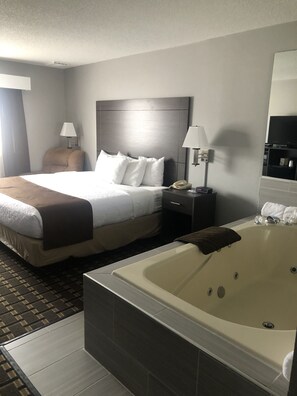 Una habitación de hotel con una cama grande, una mesita de noche con lámpara, un teléfono y una bañera.