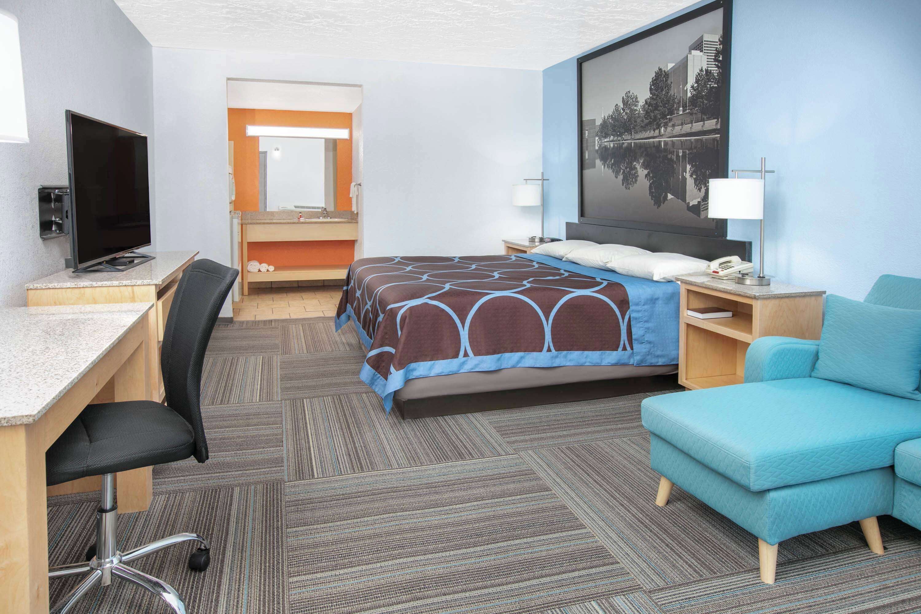 Ein Hotelzimmer mit einem Bett, einem Schreibtisch mit Computer, einem Sessel, einem Fernseher, einem Nachttisch und einer Couch.