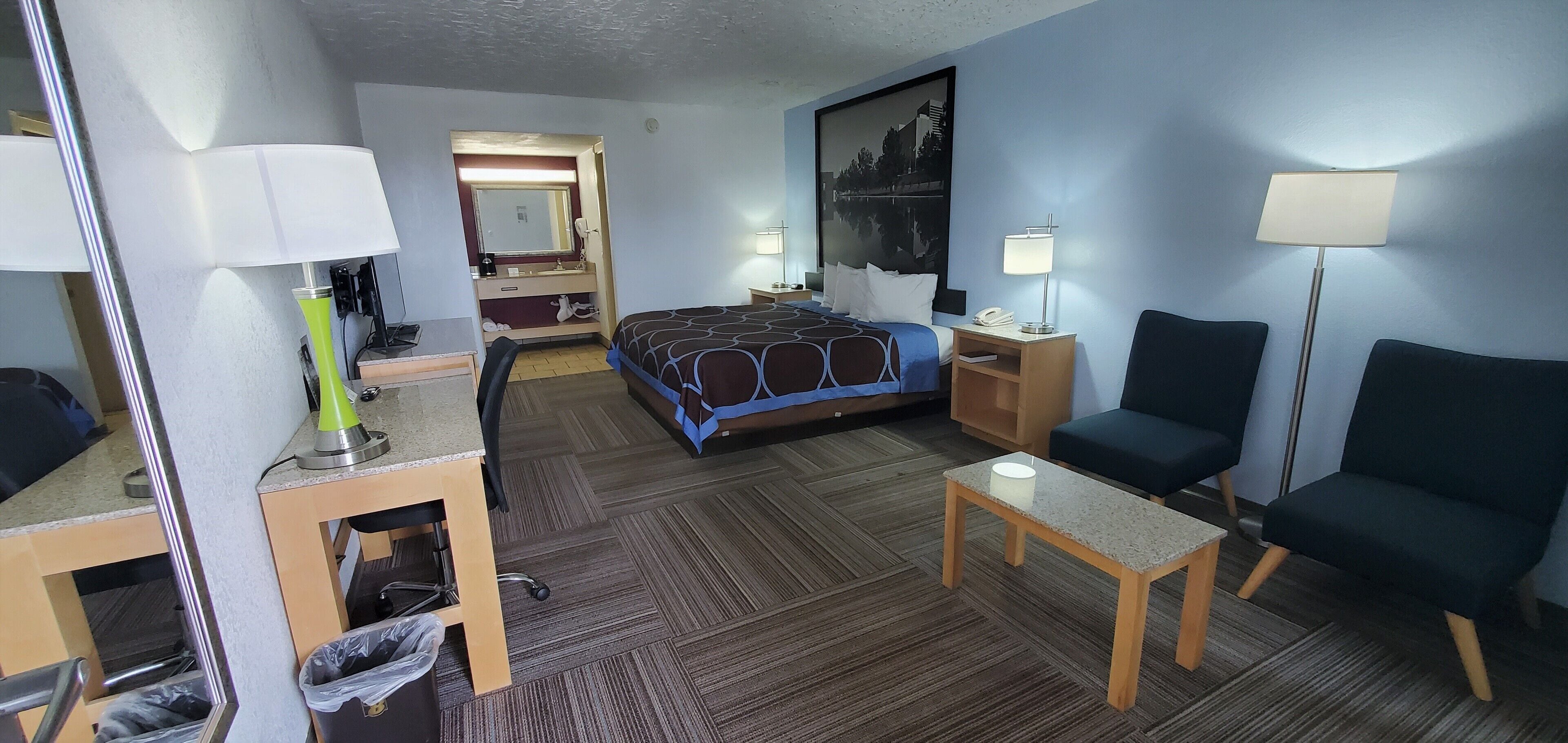 Una habitación de hotel con cama, escritorio, silla y una mesa con lámpara.