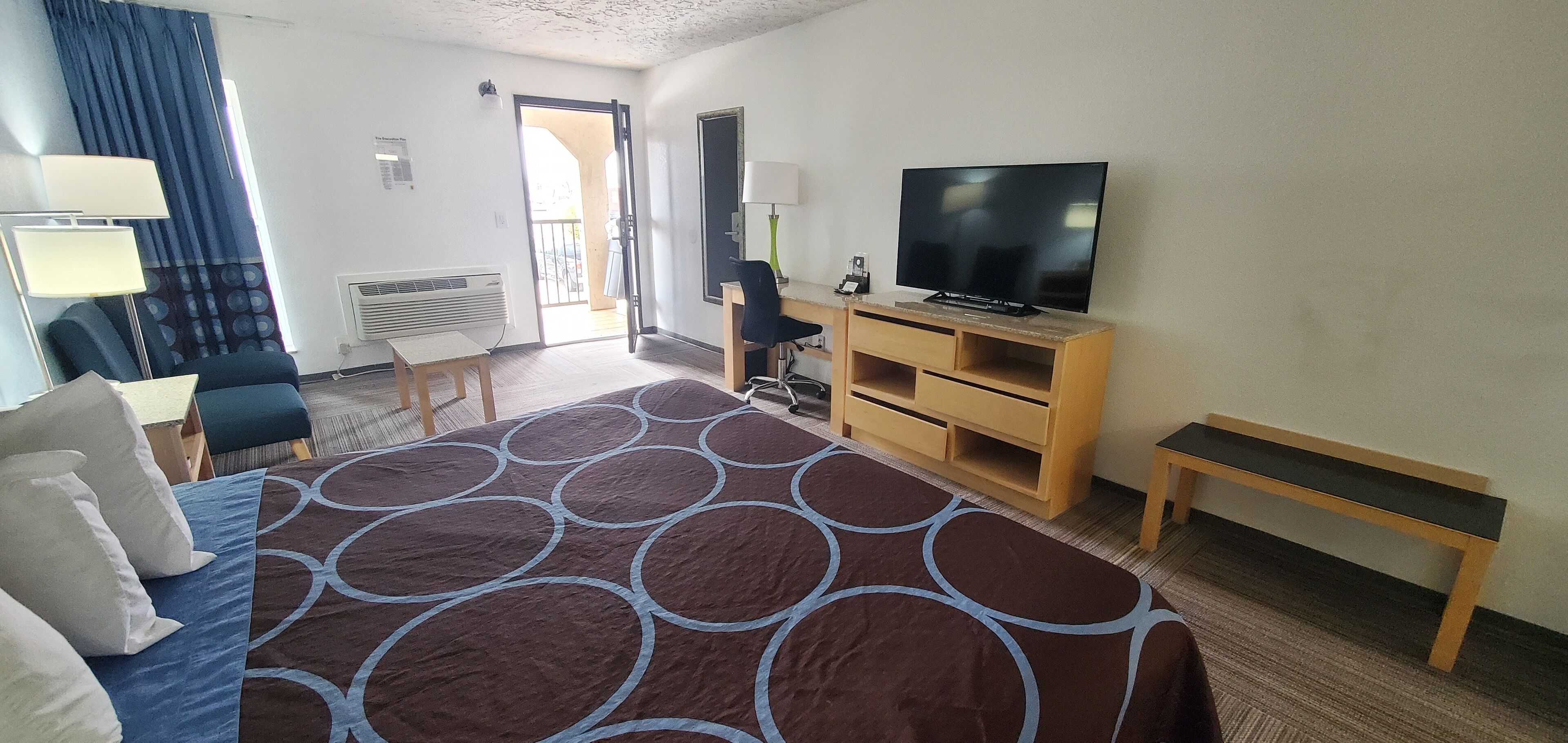 A hotel room with a large bed, a TV, a desk, and a chair.
