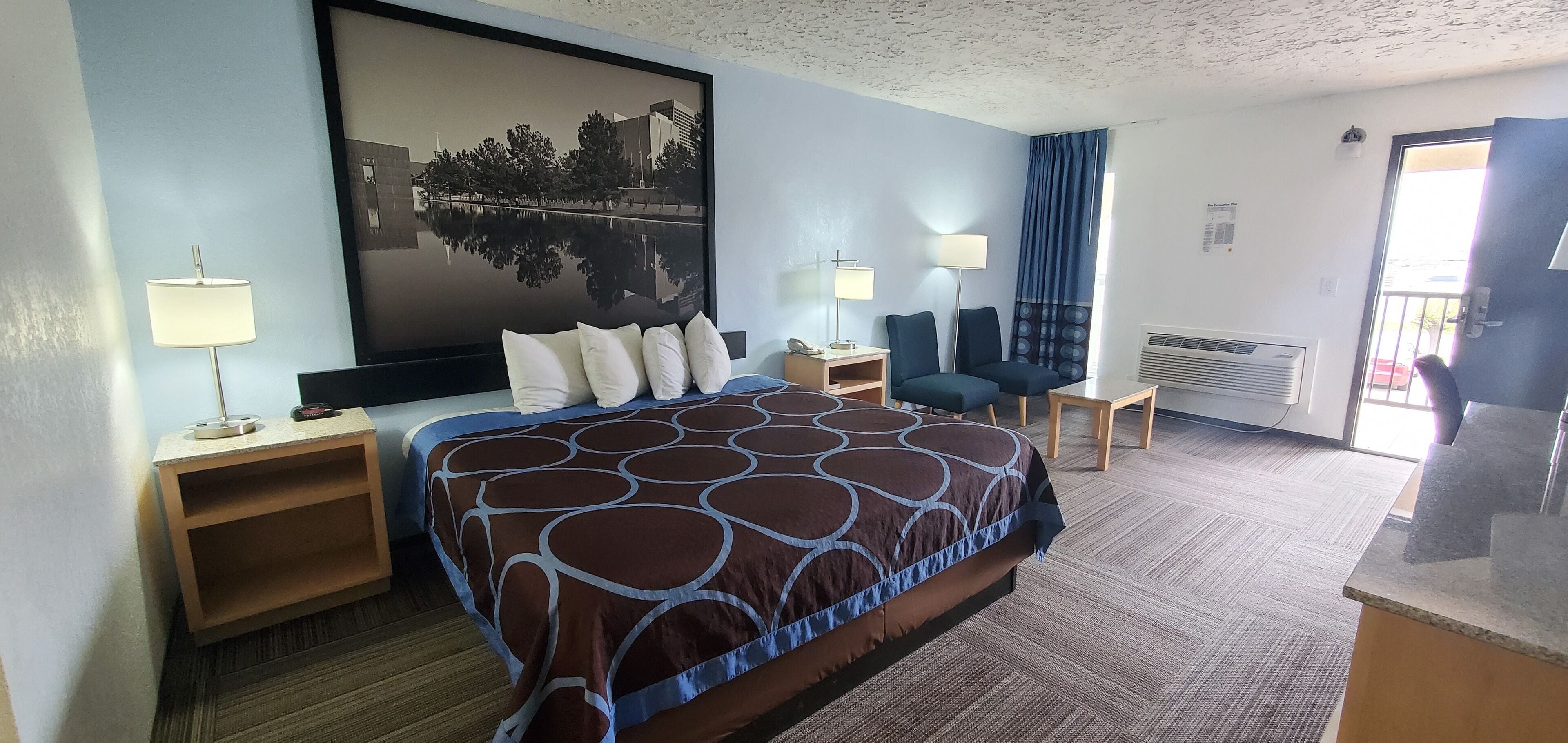 Ein Hotelzimmer mit einem großen Bett, zwei Nachttischen, einem Schreibtisch, einem Sessel und einem großen Fenster mit Vorhängen.