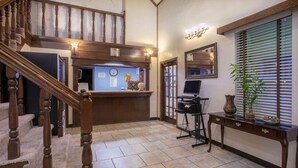 A reception area with a wooden staircase, a reception desk, a computer, and a potted plant.