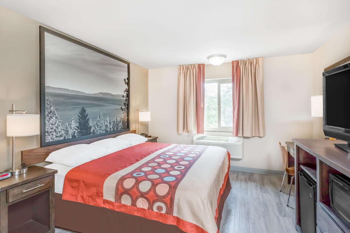 A hotel room with a large bed, a desk with a television, a window with curtains, and a painting on the wall.