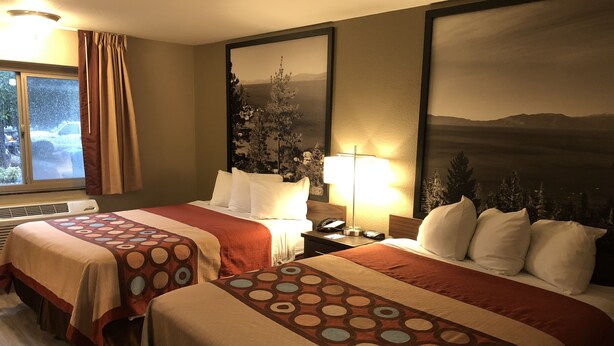 A hotel room with two beds, a window with curtains, a heater, and a wall with framed artwork. - Super 8 by Wyndham Redding (Redding)