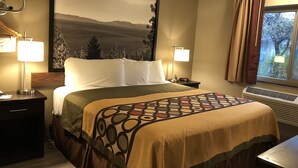 A hotel room with a bed, two bedside lamps, a nightstand, a window with curtains, and a wall-mounted air conditioner. - Super 8 by Wyndham Redding (Redding)