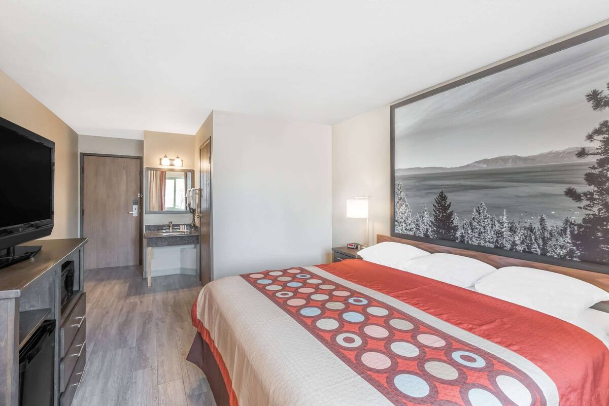 A hotel room with a bed, a TV, a bathroom, and a painting of a landscape.
