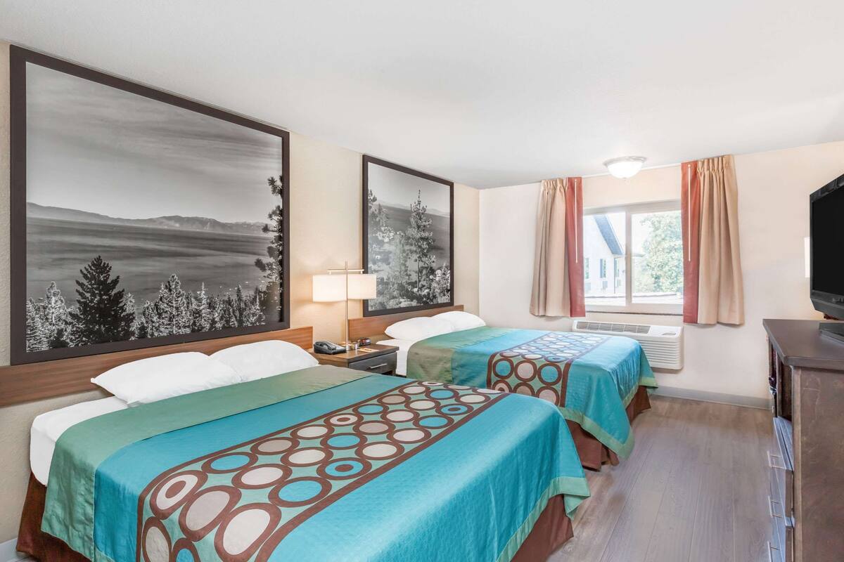 A hotel room with two beds, a TV, a desk, and a window with curtains.