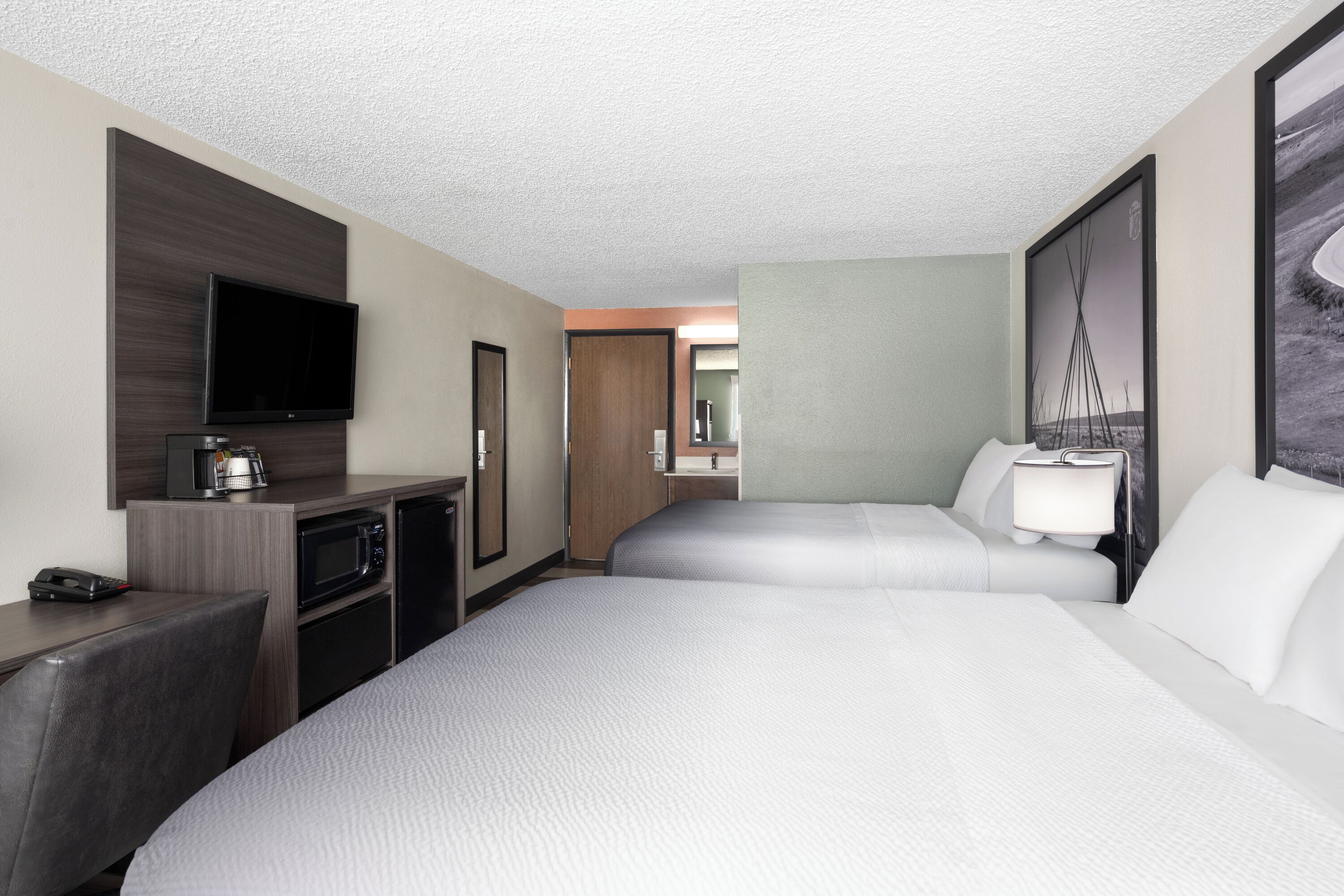 Habitación de hotel con televisión de pantalla plana, microondas, cafetera, escritorio y dos camas con ropa blanca.