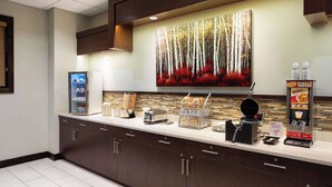A hotel reception area with a counter, a refrigerator, a coffee machine, and a large painting of trees and flowers. - Super 8 by Wyndham Conrad (Conrad)