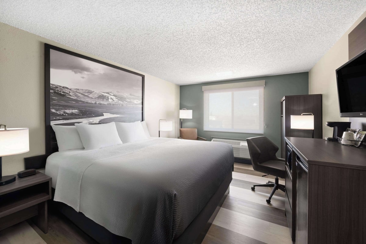 A hotel room with a large bed, a desk, a chair, and a television.